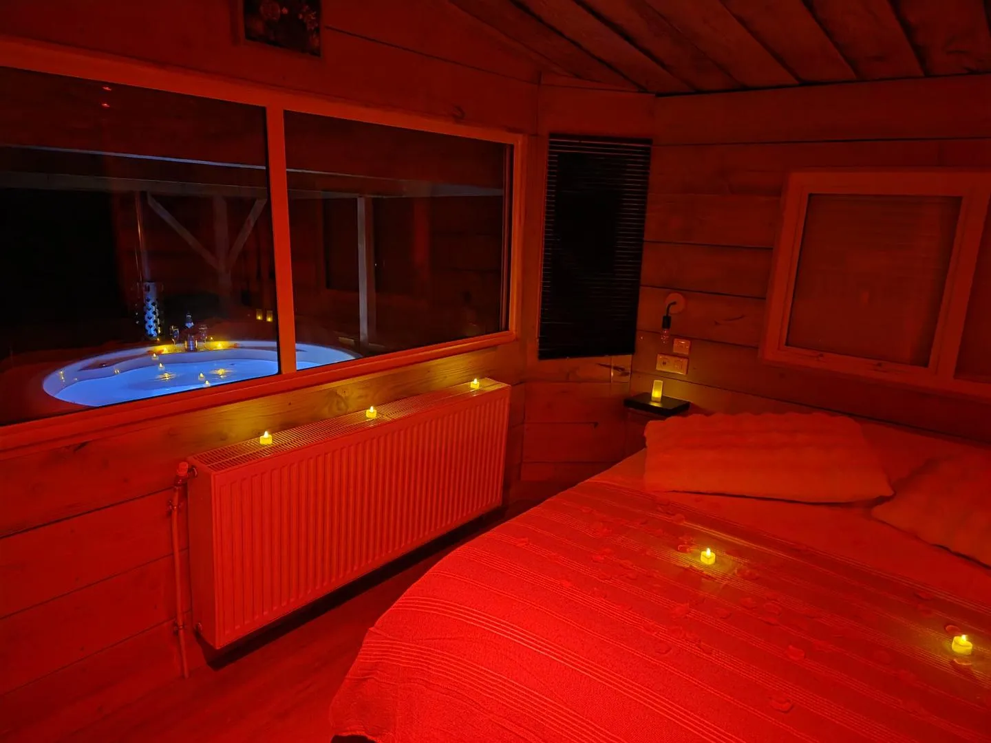 La chambre principale éclairée le soir avec le bain nordique visible par la fenêtre
